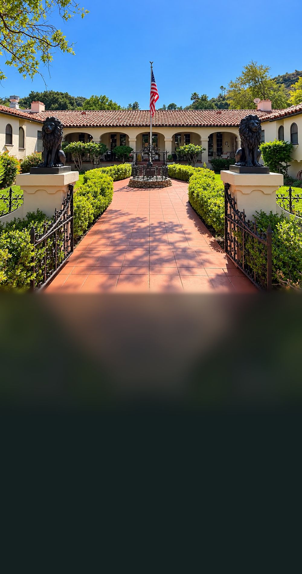 The Spanish-style courtyard entrance of Paradise of North Valley, with lion statues on the gate pillars, a brick path and the American flag