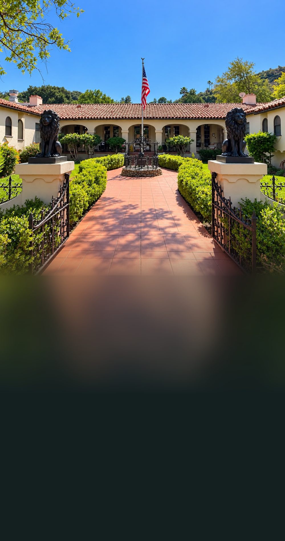 The Spanish-style courtyard entrance of Paradise of North Valley, with lion statues on the gate pillars, a brick path and the American flag